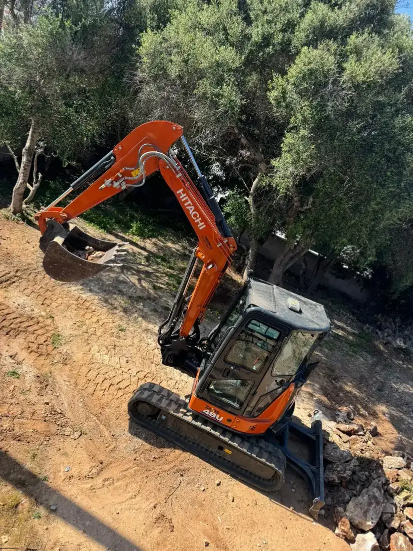 Miniexcavadora acondicionando terreno de finca entre olivos
